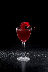 Liqueur glass with chocolate beet liqueur. Decorated with beetroot chips and chocolates on a skewer. Black background, drops of water.