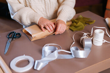 Close-up top view of unrecognizable young woman wrapping festive Christmas gift box in craft paper with presents for family and friends. Preparing for xmas, new year and winter holidays, festive mood