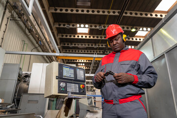Black CNC Machine Operator In Protective Workwear Checking Measurements With Vernier Caliper Next To CNC Controller - Portrait Of African American Industrial Worker