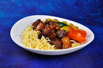Roast pork with noodles and vegetables on a plate.