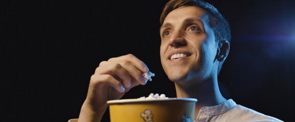 Smiling man watching a movie and eating popcorn