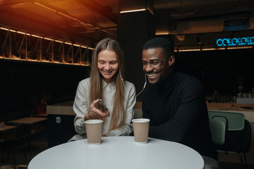 Happy friends sitting in the cafe, sharing their one pair of headphones