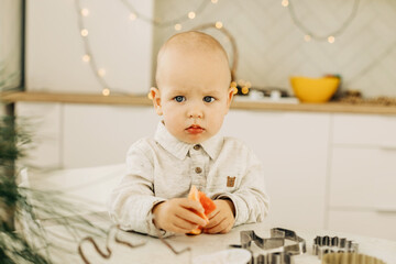 Naklejka premium A sad kid with a grapefruit in his hands is sitting at a table with cookie cutters on it. Preparing for the holidays, Christmas Eve or New Year's Eve
