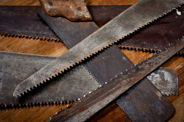 Old vintage metal saws for wood of different shapes and sizes, crumpled on a wooden background.