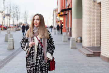 Young woman on the street of the city. Beautiful smiling blonde in a warm stylish coat.