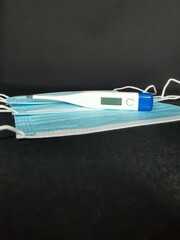 Medical masks and thermometer on black background