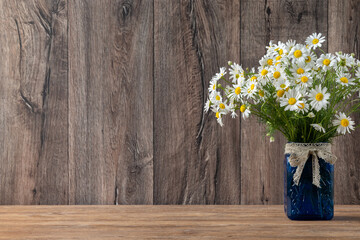 Bouquet of daisies in blue jar on dark rustic wooden background with copy space