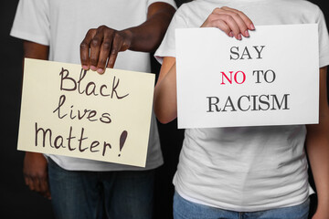 Young woman and African American man holding signs on black background, closeup. Racism concept