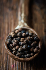 Black pepper on an ceramic spoon over wooden backround