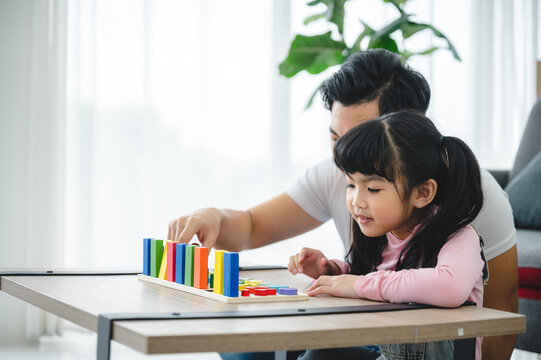 Cheerful and playful cute little girl learning numbers and math with handsome young father at father by playing with blocks for educational development at home