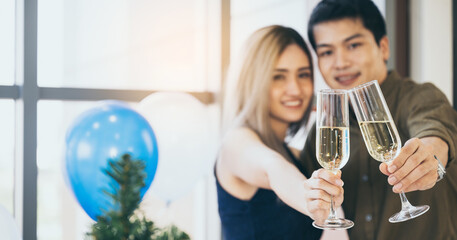 Closeup of hands of handsome man with beautiful woman celebrating and enjoying occasion with champagne and raising a toast while hugging and looking at camera at a decorated room with balloons