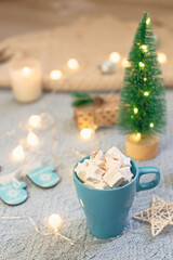Obraz na płótnie Canvas A blue mug with cocoa marshmallows, blue background of Christmas decor, stands on a knitted blue blanket.