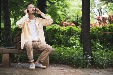 Handsome young Asian man listening nd enjoying to soulful music with headphones and closed eyes...