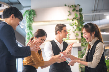 Young beautiful smiling woman giving sanitizer to man with a group of people rubbing and sanitizing their hands before entering the venue