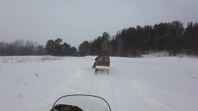Steadicam shot of snowmobiles ride in the field to siberian forest. Camcorder following the forward snowmobile