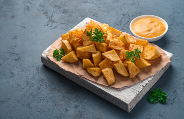 Fried potatoes with sauce on a white board, patatas bravas on a dark background.