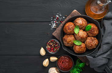 Fried meatballs on a black background with sauce and spices