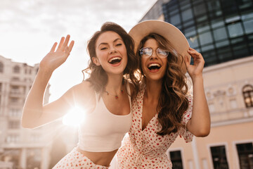 Bottom view of two cheerful beautiful caucasian young women posing for photo in sunbeams. On warm...