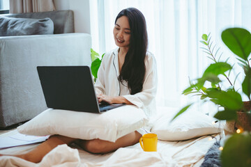 young Asian woman using laptop computer to business online work, female freelance working from home by using internet cyberspace communication technology for businesswoman job