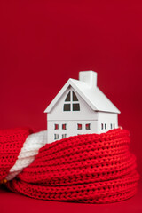 White toy house wrapped in red scarf on red background. Heating or insulating buildings concept,...
