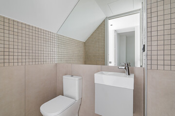 Interior of modern bathroom with beige tiles, toilet and small sink