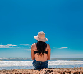 woman in hat from back to the sea, girl in hat looking to the sea, vacation concept, rear view of a girl watching the sea