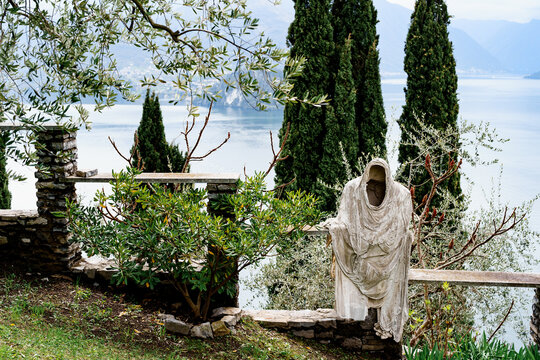 Ghost statue on a stone fence among green trees on the shores of Lake Como. Italy