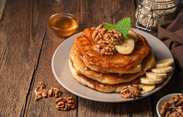A stack of pancakes with honey and nuts on a wooden background.