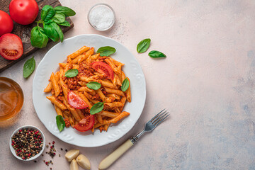 Penne pasta with tomato and meat bolognese sauce and fresh basil on a beige-pink background.