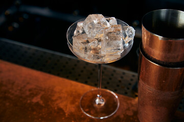 Large glass filled with ice cubes next to the shaker