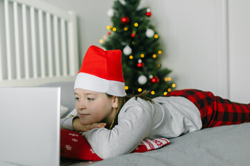 Caucasian girl in santa hat looking at laptop, watching movie. Concept of home christmas lifestyle.