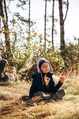 Naklejka na ściany i meble A boy in warm clothes meditates in the forest while sitting on the grass while walking. Portrait of a child