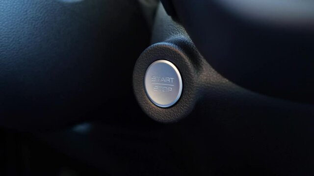 Man uses finger with nail cut unevenly to press start-stop silver-colored button on black plastic dashboard of expensive foreign car closeup