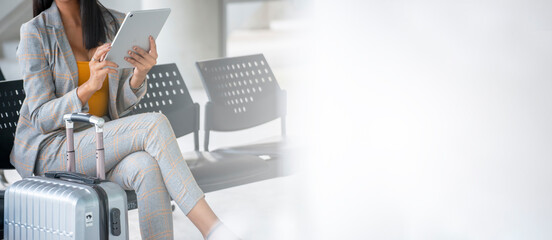 Businesswoman sit and wait at passenger boarding terminal in airport, luggage and suicase bag on the side. Woman travel to work and using tablet to find hotel. Domestic Travel concept-panoramic banner