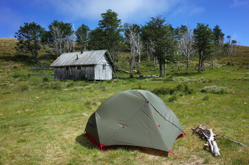 Tent on green grass by old wooden house and small forest on hill, Summer vacation, Camping at...