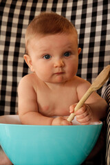 Cute happy little boy with blue eyes playing with spoon and bowl