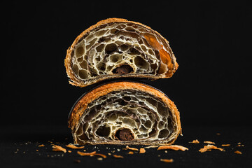 A chocolate croissant cut in half showing the filling and layers of pastry, on black background