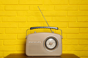 Retro radio receiver on wooden table near yellow brick wall