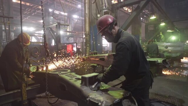 Busy Workshop Room at the Industrial Factory. Two Workers are Operating the Grinding Tools. Grinding a Metal detail at the Workshop. Production Process at the Workshop. Industrial Manufacturing