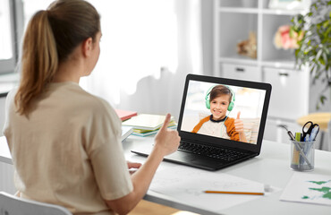 Fototapeta na wymiar distant education, remote job and e-learning concept - female teacher with laptop computer having video call or online class with smiling student boy in headphones at home office and showing thumbs up