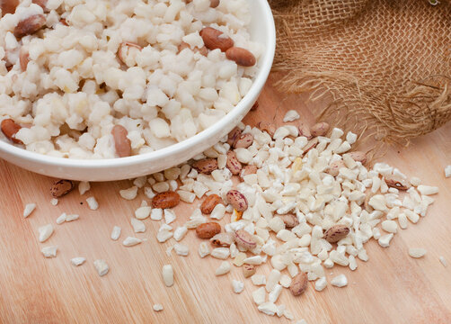 South African staple of pounded maize kernels known as samp and beans. bowl of cooked samp on wooden table with burlap and farmstyle feel with raw samp and copy space