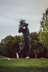 Golfer swinging with trees in the background on a cloudy day