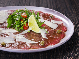 Marbled beef carpaccio with arugula, lemon and parmesan cheese on light plate
