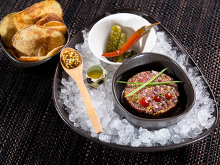 fresh beef tartare, raw minced meat with capers, chopped onion and dijon mustard  in a bowl on ice bed