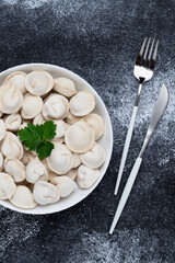 A bowl of dumplings with fork and knife on dark table. Top view. Food background. Pelmeni is a traditional dish of Russian cuisine.