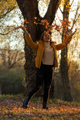 Naklejka premium Girl throwing leaves in the air. Autumn landscape. Yellow jacket and gray sweater.