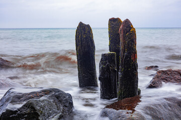 Verwitterte Holzpfähle und Felsen in der Brandung der Ostsee – kraftvolle Küstenlandschaft mit...