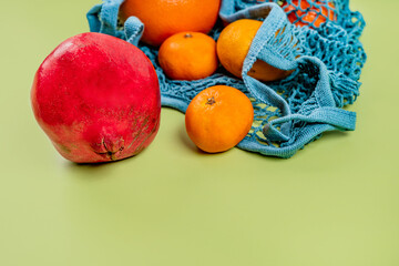 Tangerines, grapefruit and pomegranate fruits lie in a cotton eco-bag on a green background. The concept of a healthy lifestyle and freshness