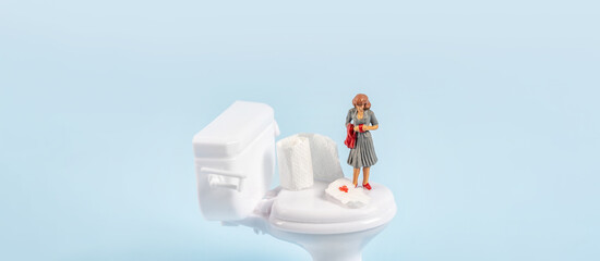 A miniature model of a woman stands near a toy toilet with toilet paper with blood. The concept of hemorrhoids