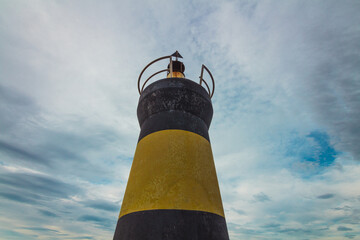Black and yellow lighthouse with cloudy sky in the background